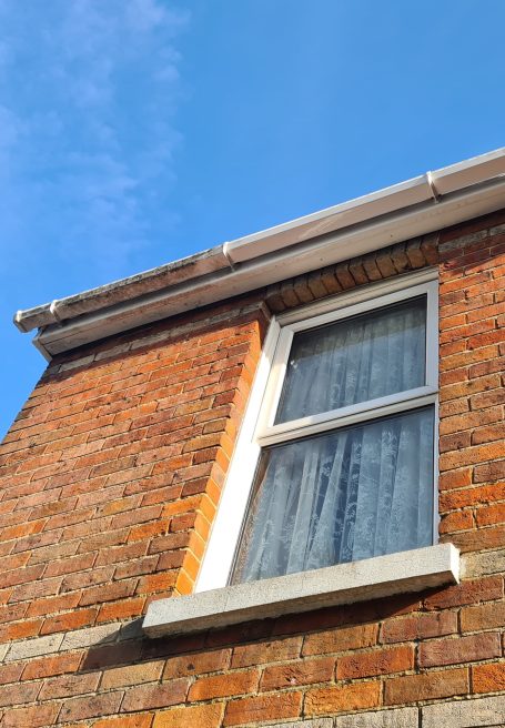 Close-up of a window on a brick house with a clear blue sky above.